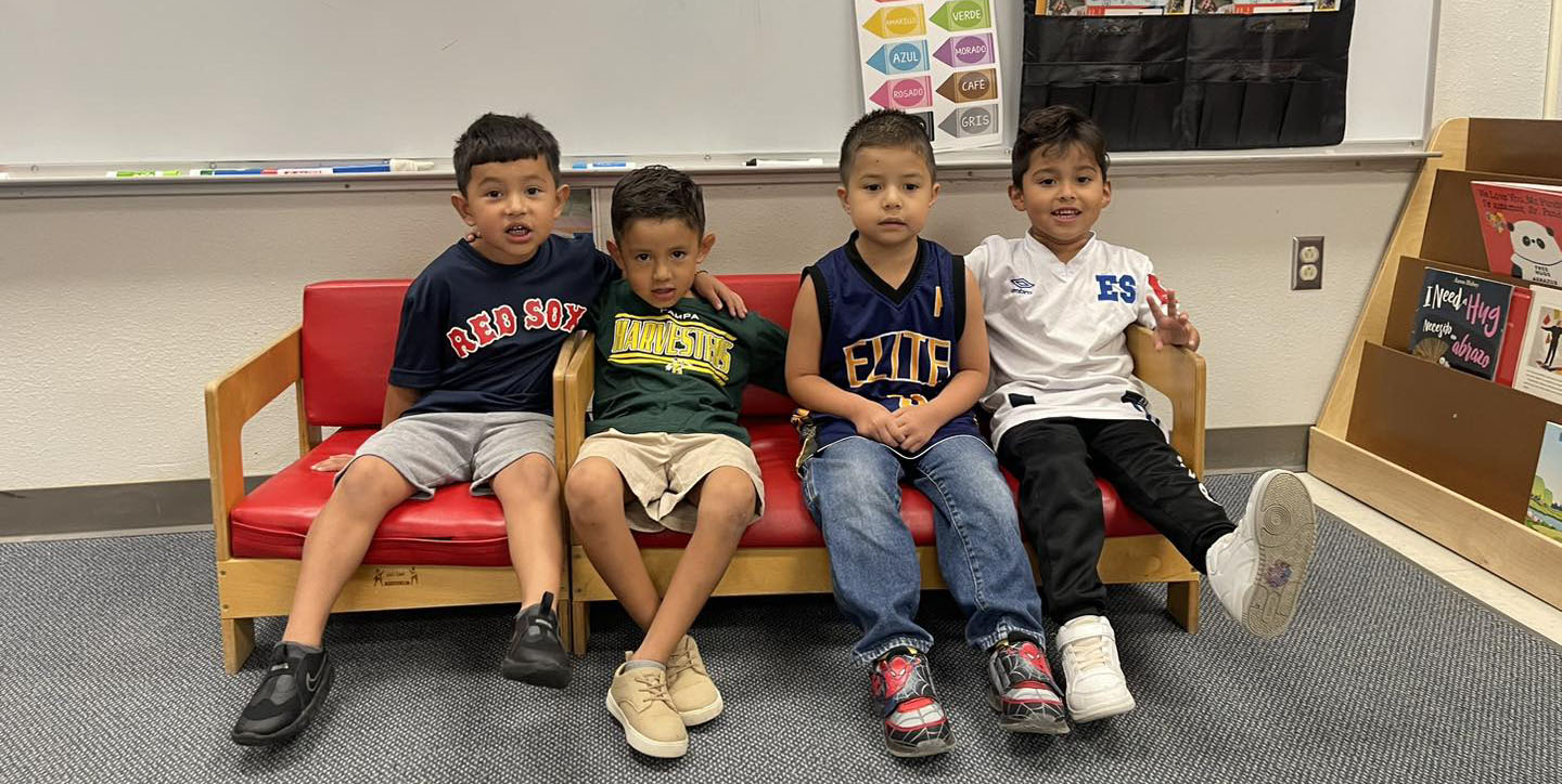 four boys sitting on small couch smiling.