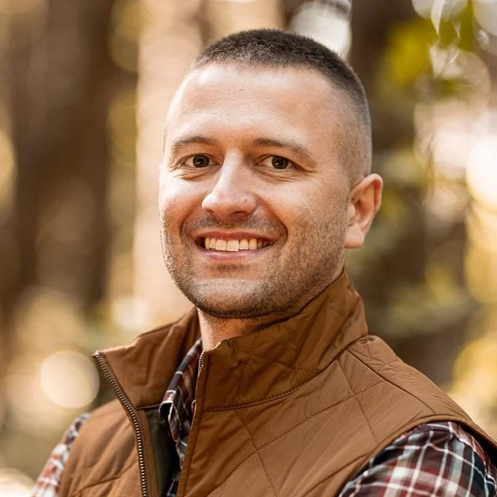 photo of man smiling in brown vest flannel shirt and buzzcut