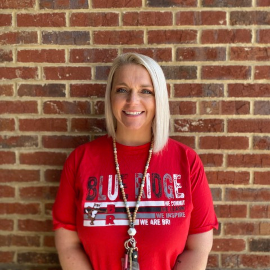 Teacher standing in front of brick wall, smiling at the camera