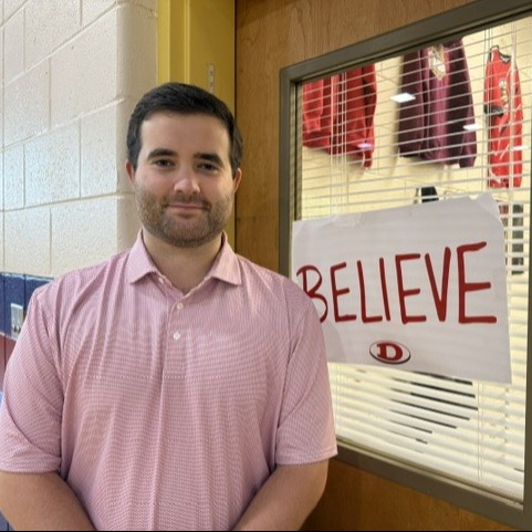 Male teacher smiling standing next to a door