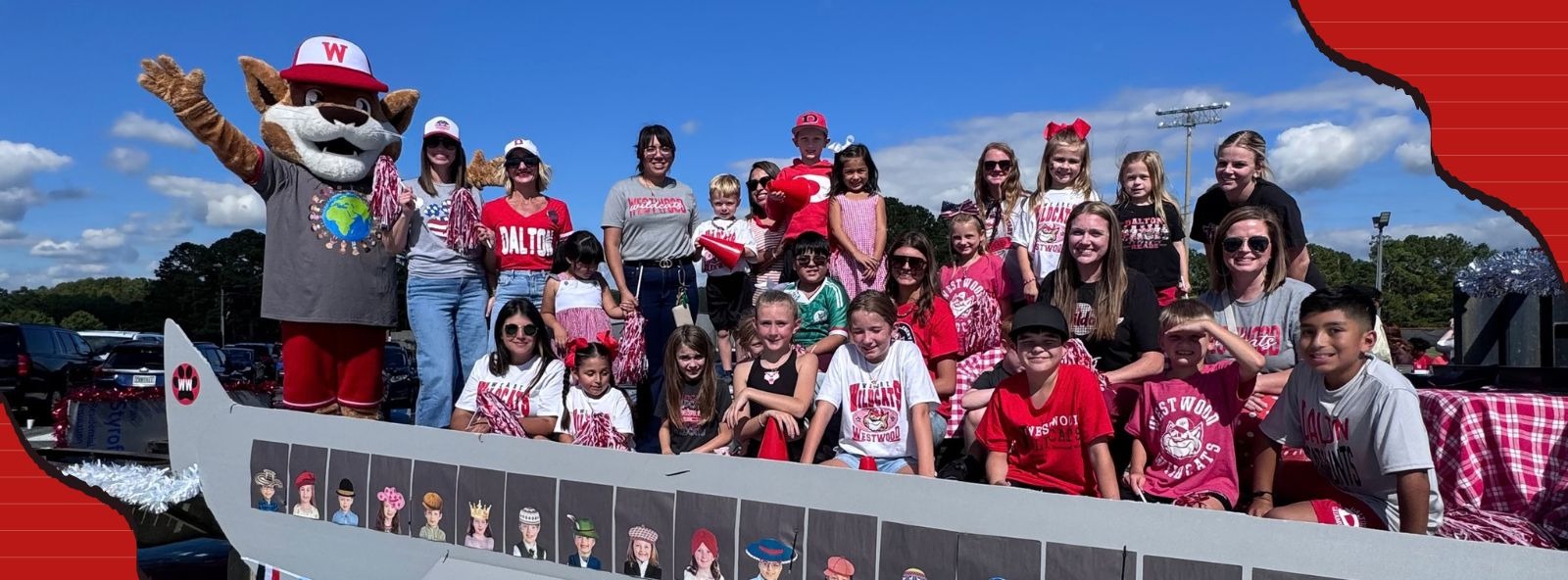 A parade float styled to look like an airplane decorated with school spirit signs reading "WILDCAT", "WESTWOOD", and "DALTON". A group of adults and children are riding on top of the float alongside a wildcat mascot wearing a hat labeled "W" and waving to the crowd. The float features photos of children framed inside fake airplane windows along its side.