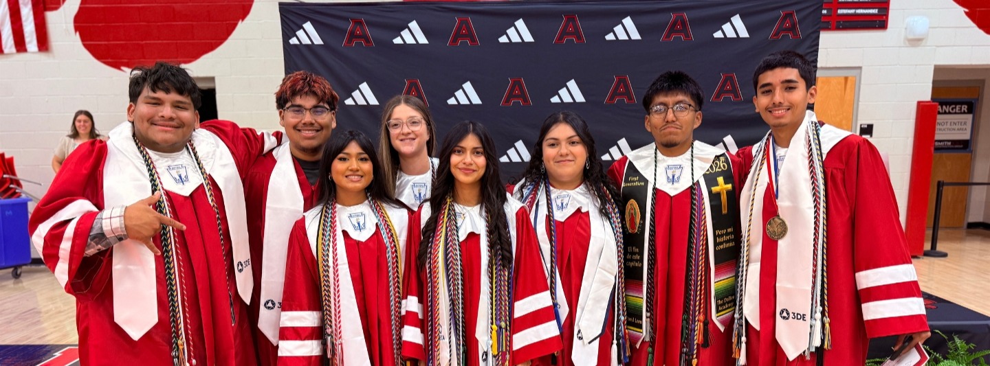 A group of graduate stands together, wearing robes