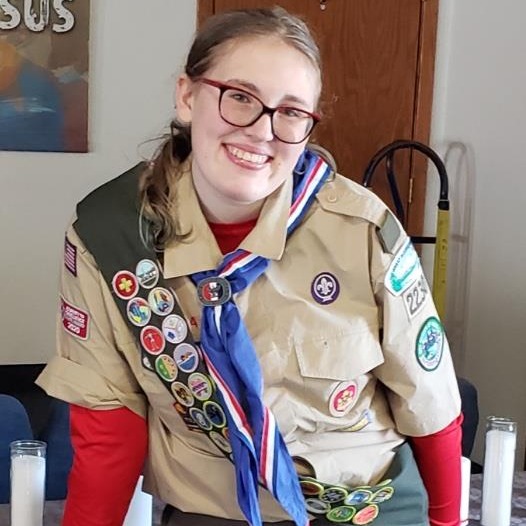 A girl scout in uniform stands confidently in front of a table, ready to engage in scout activities.