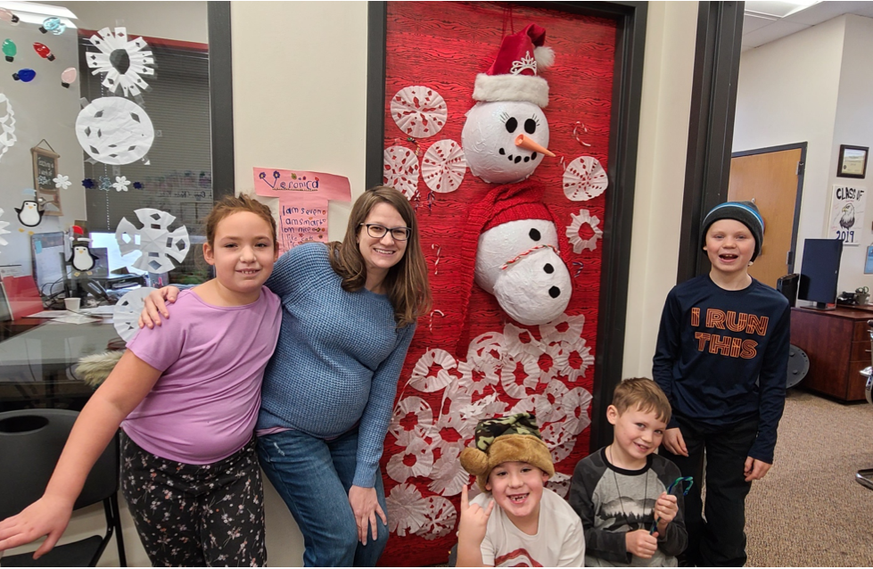 A group of children smiling and posing for a photo in front of a door adorned with snowflakes.