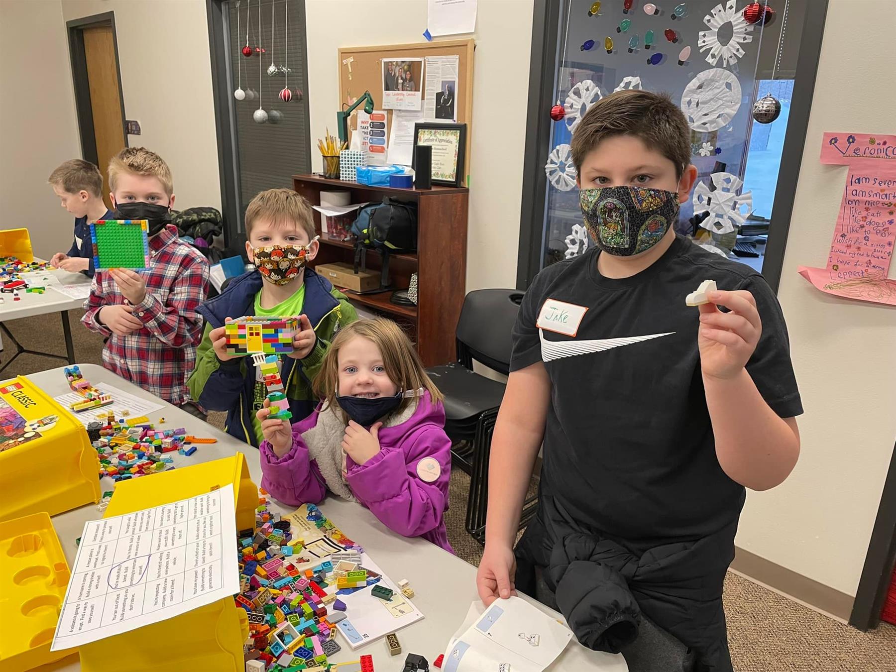 Children wearing face masks and holding lego pieces, promoting safety and creativity during playtime.