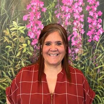 Woman standing in front of colorful flower wall, smiling.