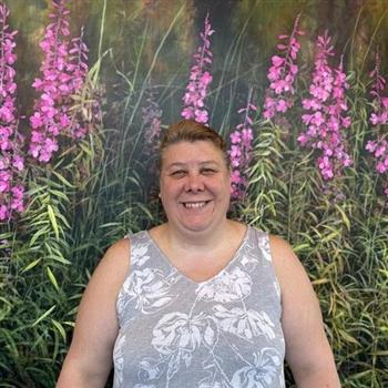 A woman standing in front of a wall of colorful flowers.