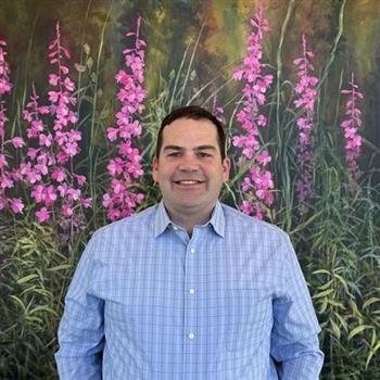 Man in blue shirt standing in front of flower painting.