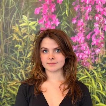 Woman in black shirt standing in front of a wall of flowers.