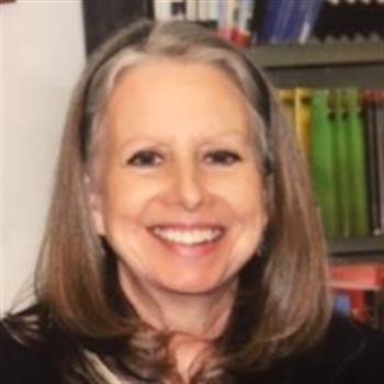 A woman with long hair and a black jacket standing confidently.