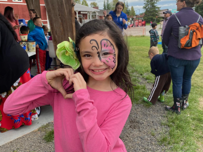 A young girl smiling with butterfly face paint on her face.