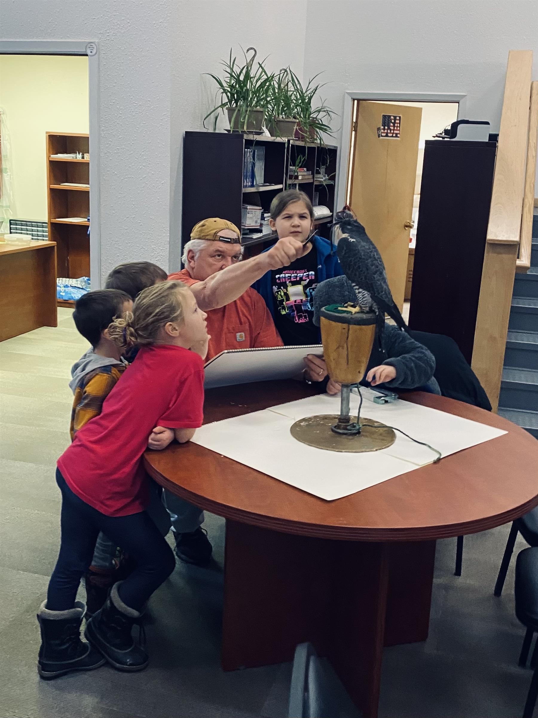 A group of children sitting around a table with a bird perched on it, engaging in an activity.