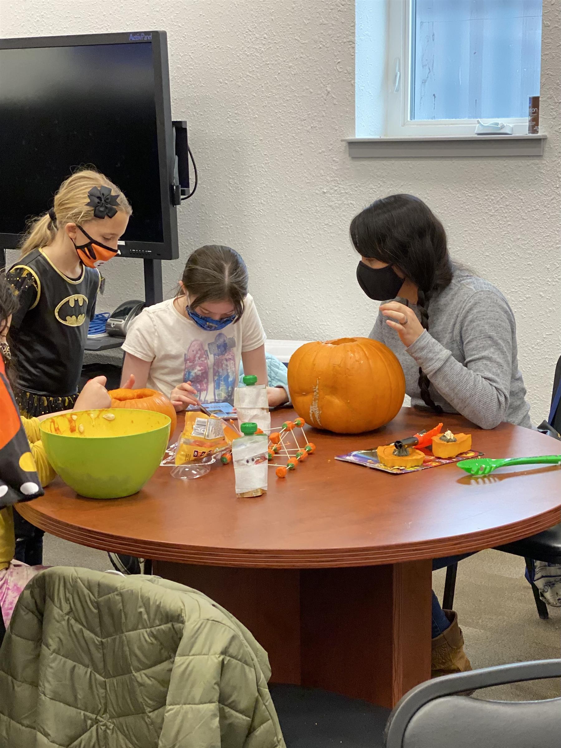 Children in various Halloween costumes sitting around a table, ready for a festive celebration.