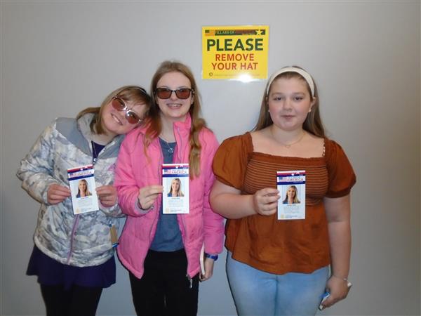 Three girls smiling and holding up cards.