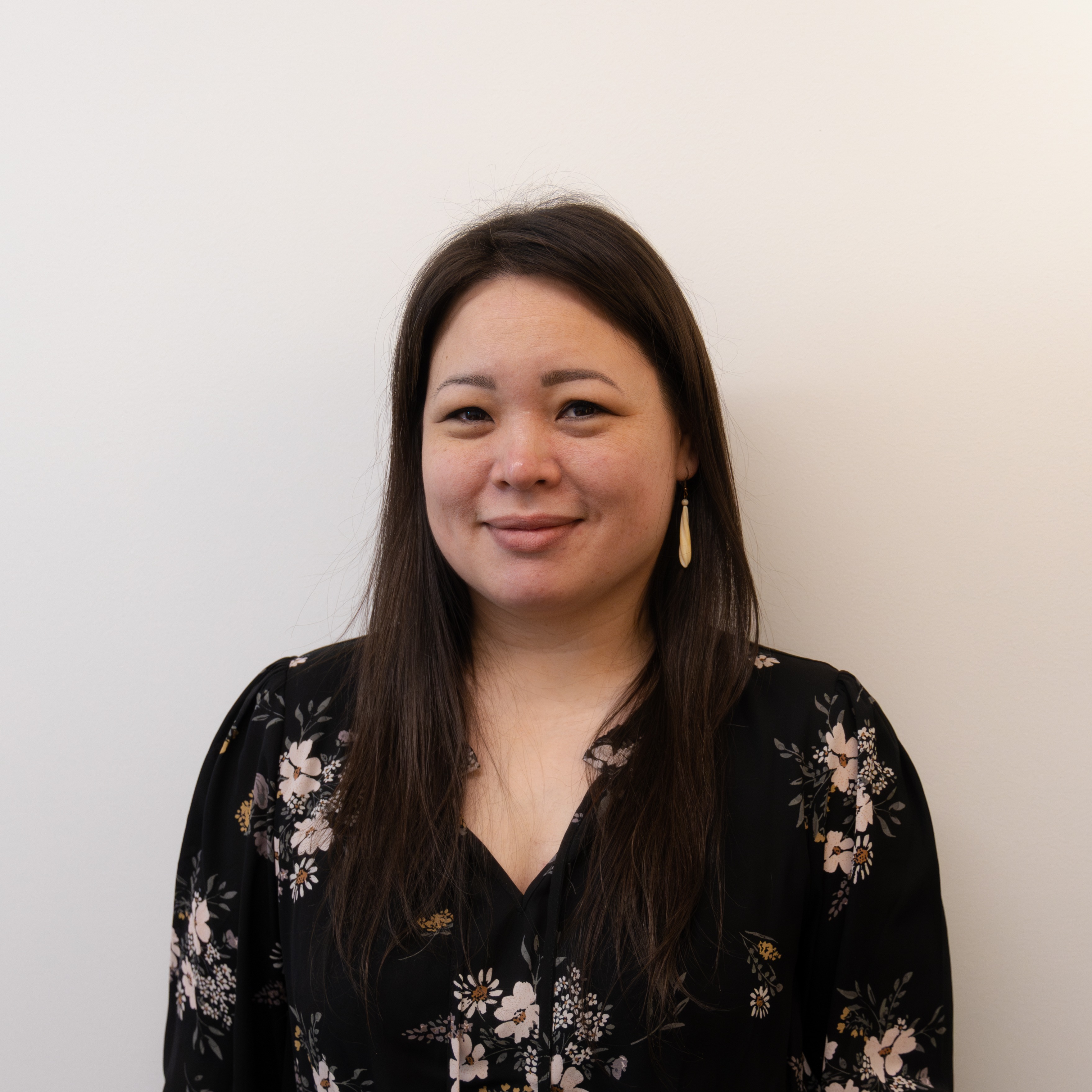 A woman with glasses stands before a vibrant wall of flowers, creating a beautiful and colorful backdrop.