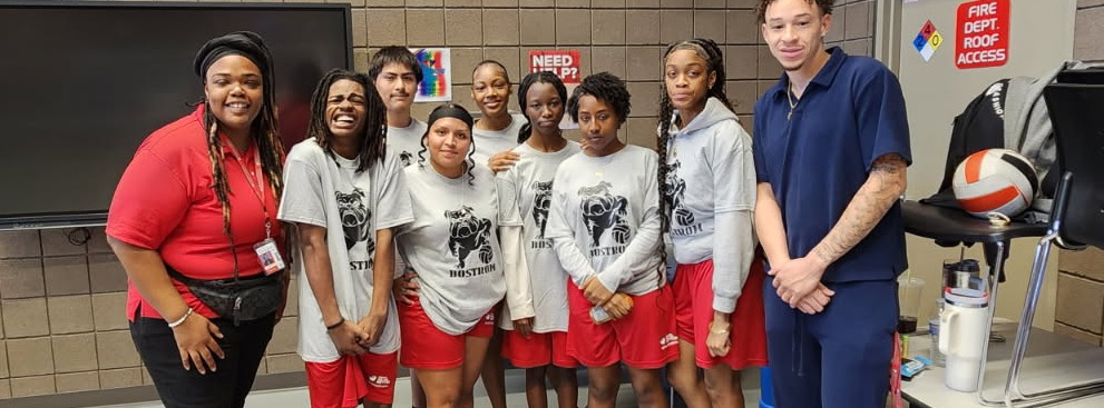 Group of people in sports gear posing with a coach in a gymnasium with flags.