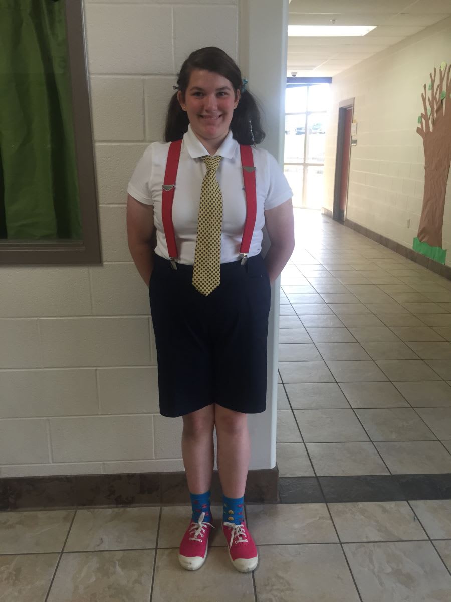 A woman wearing a tie and suspenders standing in a hallway