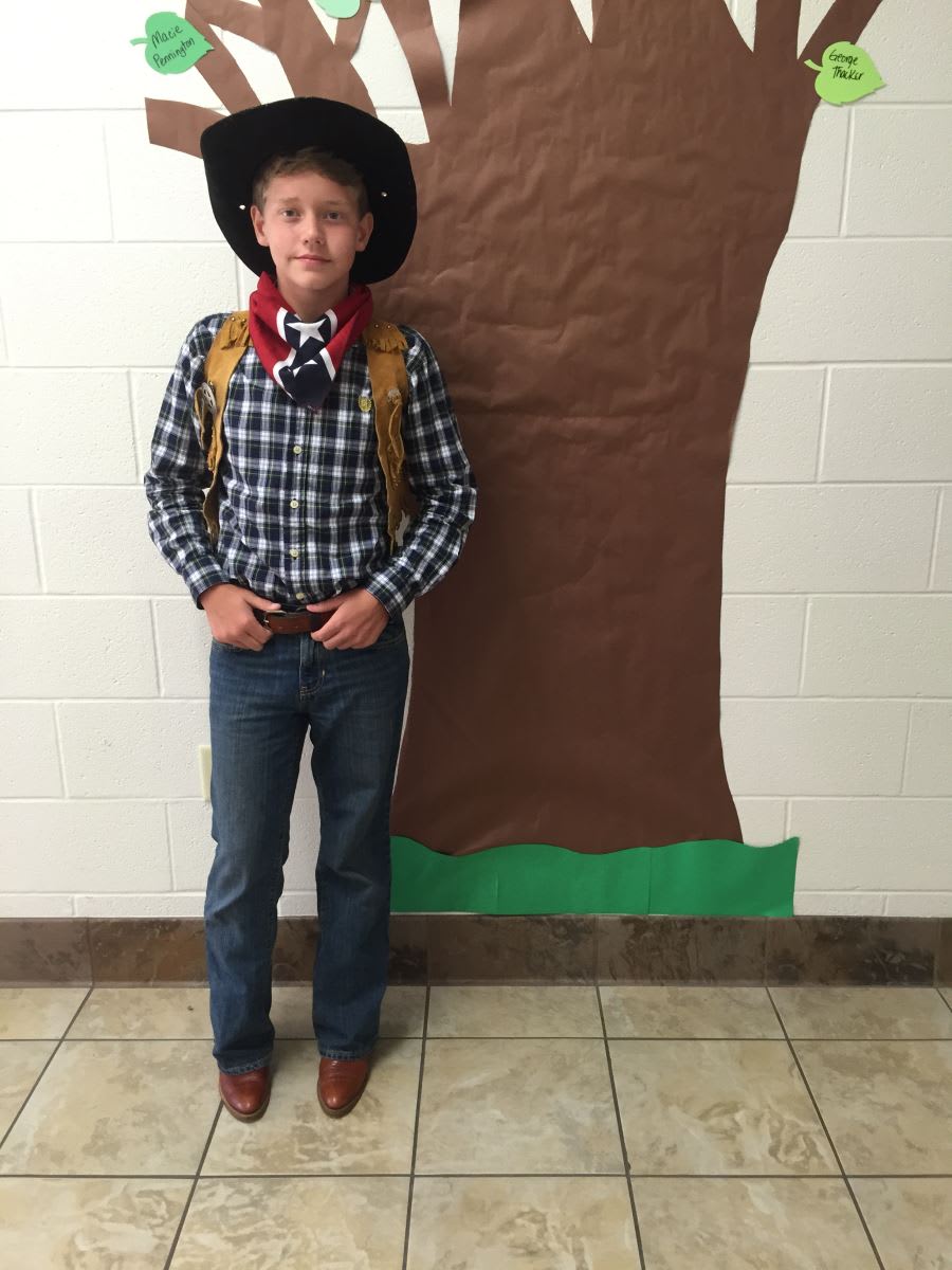 A young boy wearing a cowboy hat standing in front of a tree