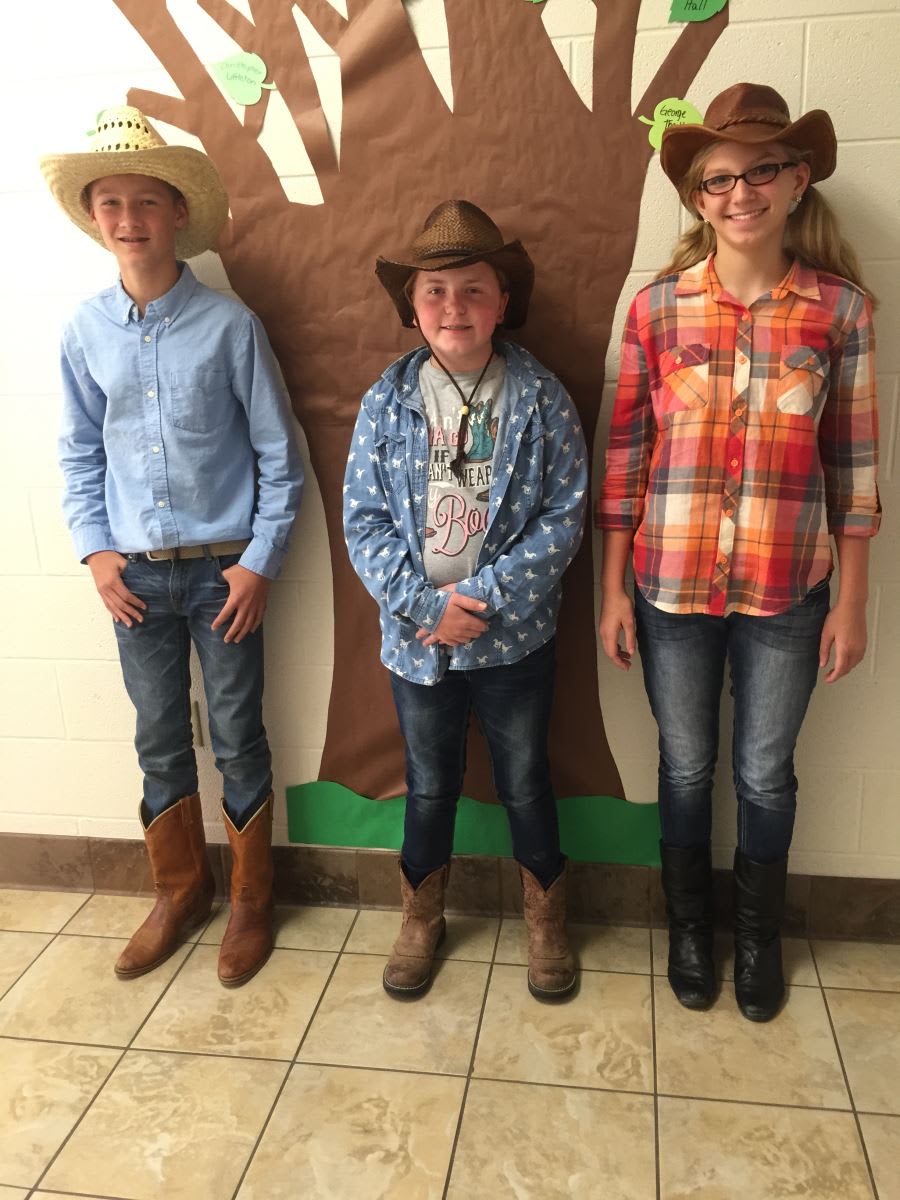 Three children in cowboy hats standing in front of a tree