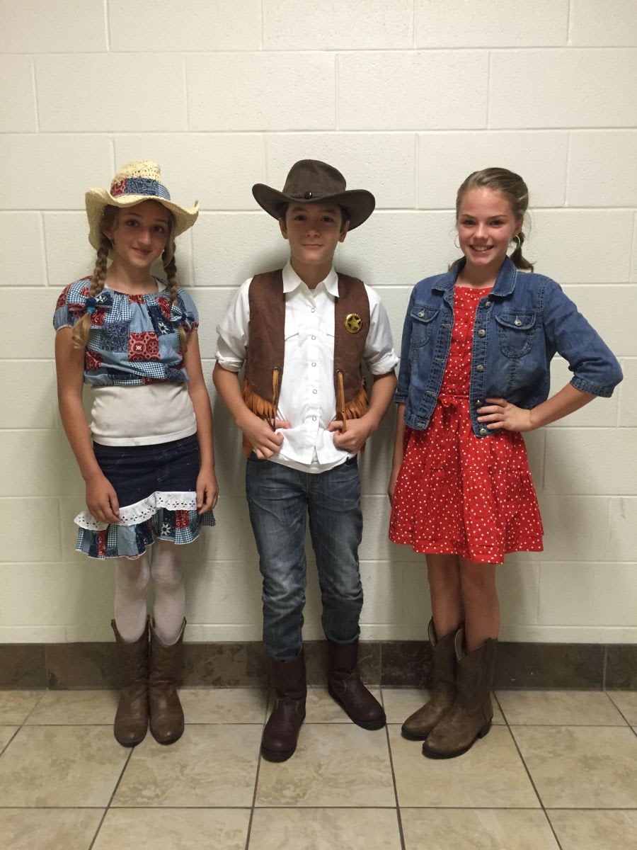 Three children wearing cowboy hats standing in front of a wall