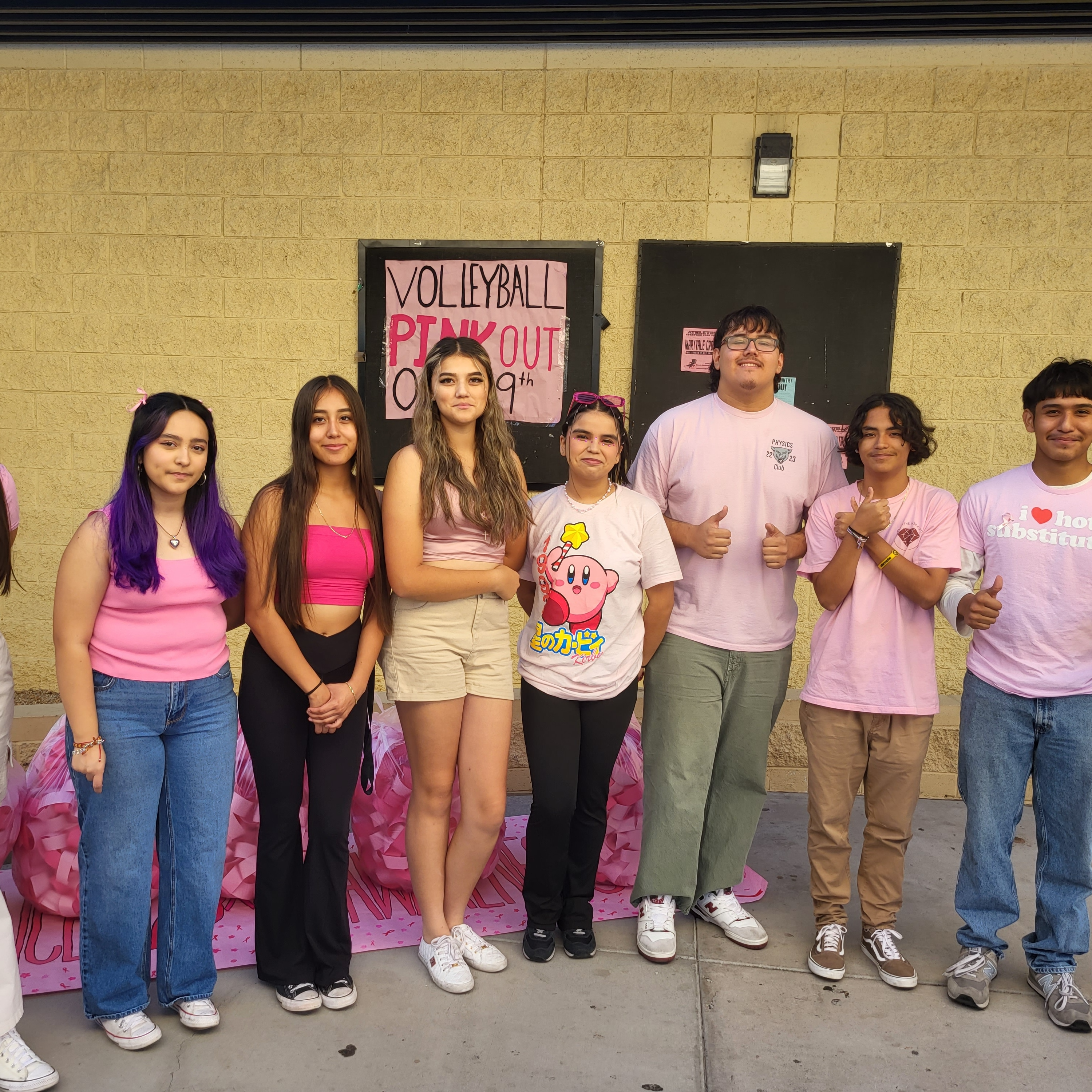 A group of people posing in front of a classroom, each holding up a face mask with different sayings written on them.