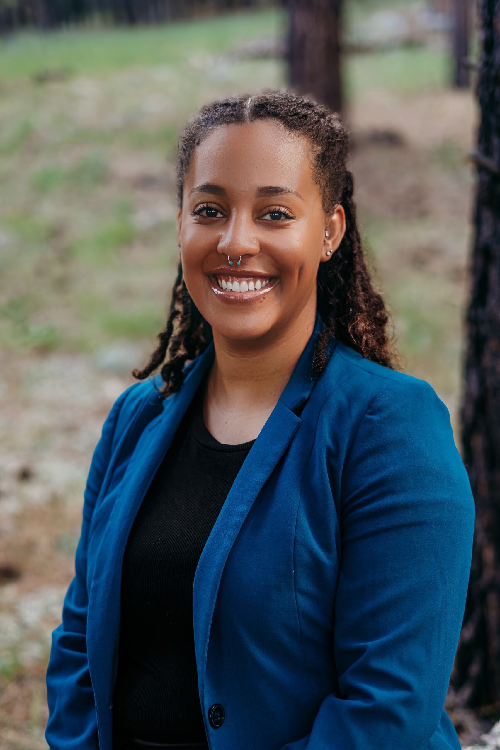 photo of smiling woman in blue blazer with forest background