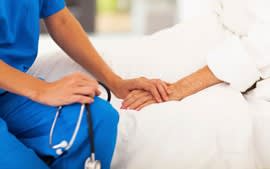 Nurse comforting elderly woman by holding her hand.