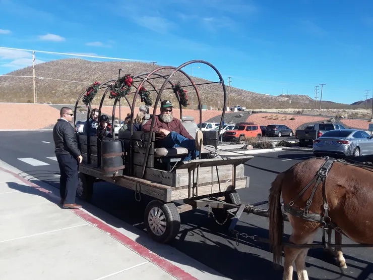 A man driving a horse-drawn carriage through a parking lot.