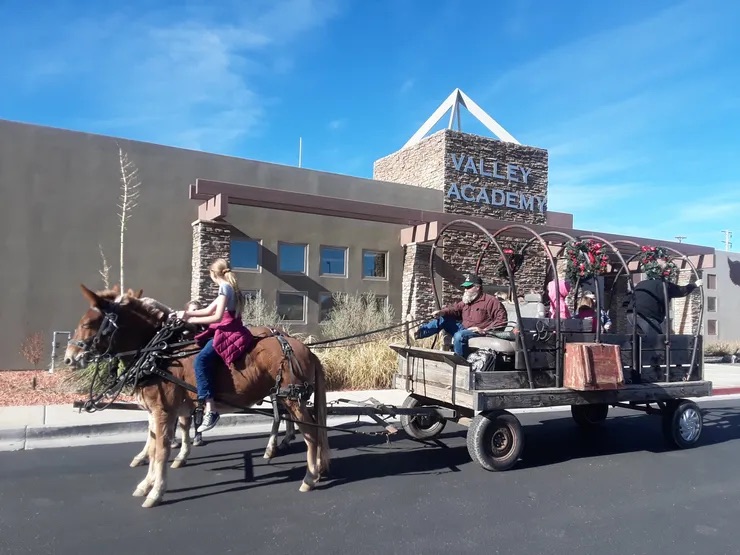 A woman riding a horse-drawn wagon through a parking lot in front of the Vale Academy building.