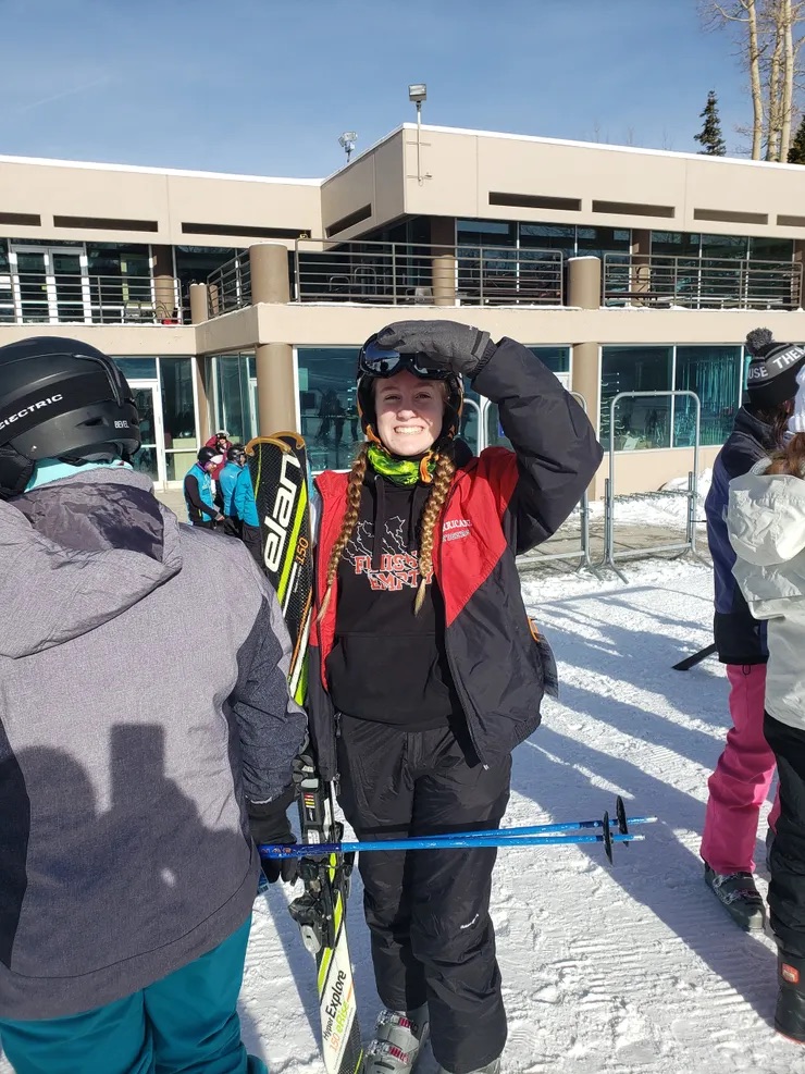 Young woman holding skis, looking upwards with a smile on her face.