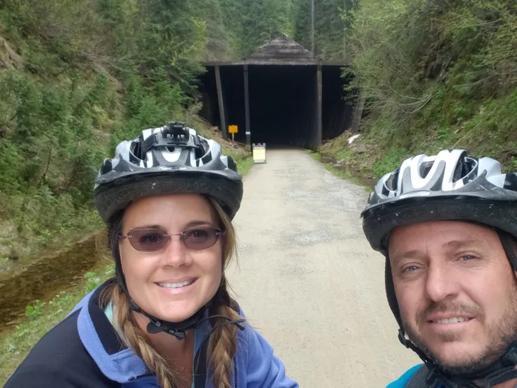 A couple on a bicycle ride, posing for a photo near a tunnel entrance.