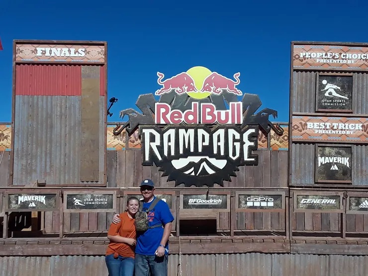 A couple posing in front of a Red Bull Rampage sign.