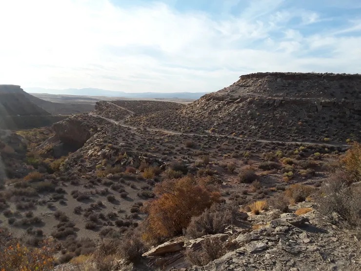 A serene landscape with a dirt road leading to a mountainous horizon under a clear sky.