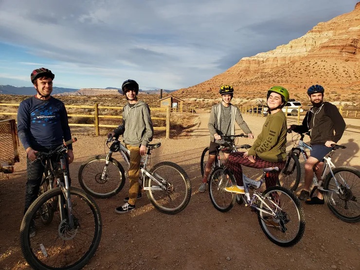 A group of bicyclists posing for a picture in front of a scenic mountain backdrop.
