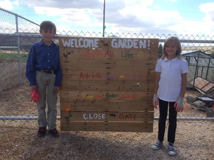 Two children standing in front of a wooden sign that says 'Welcome to Garden!'