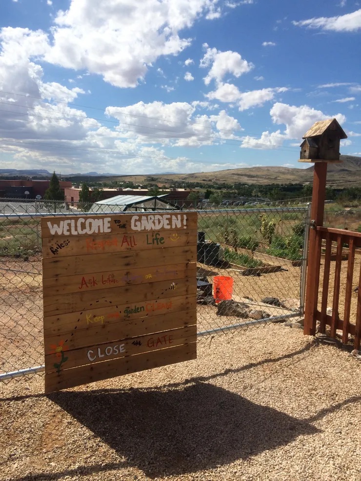 Welcome to our garden" sign on a wooden fence, with a fenced-in area beyond.