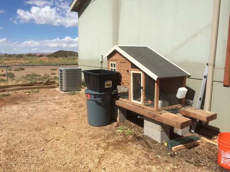 Chicken coop with a small dog house beside it, both located in an outdoor area.