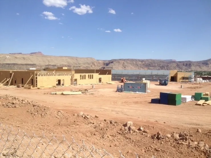 This is a photograph of an empty construction site with partially completed buildings, under a clear blue sky.