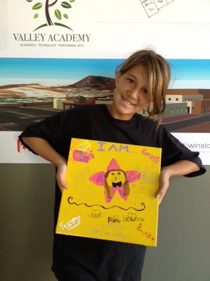 A young girl proudly holding a painting of herself with her signature, showcasing her artistic talent.