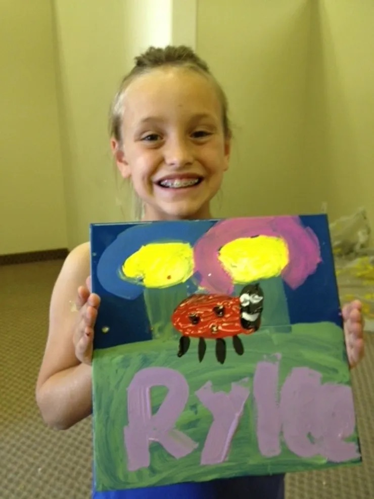 A young girl proudly holding up a colorful painting of a caterpillar.
