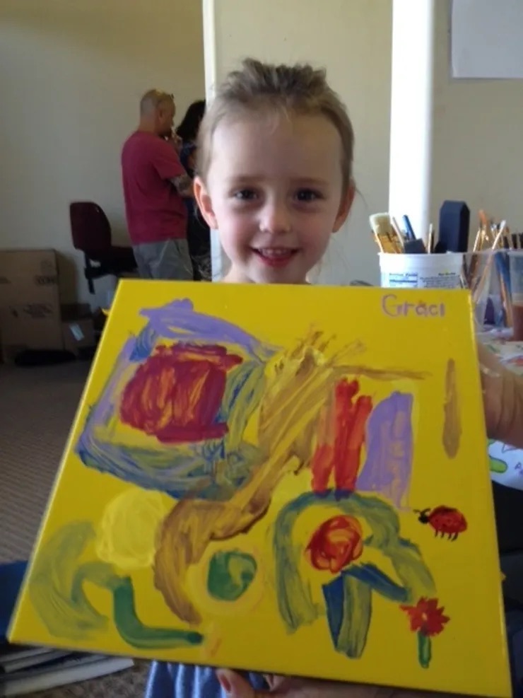 A young child holding a painting with colorful strokes.