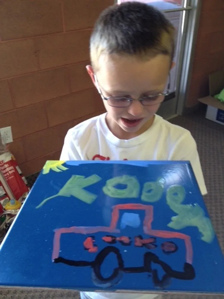 A young boy proudly showing off his artwork depicting a truck.