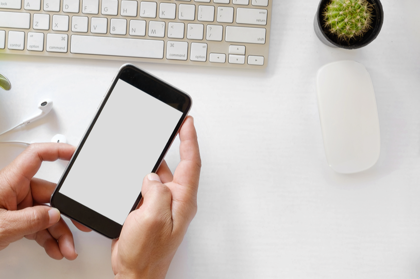 person holding a cell phone at a desk with computer