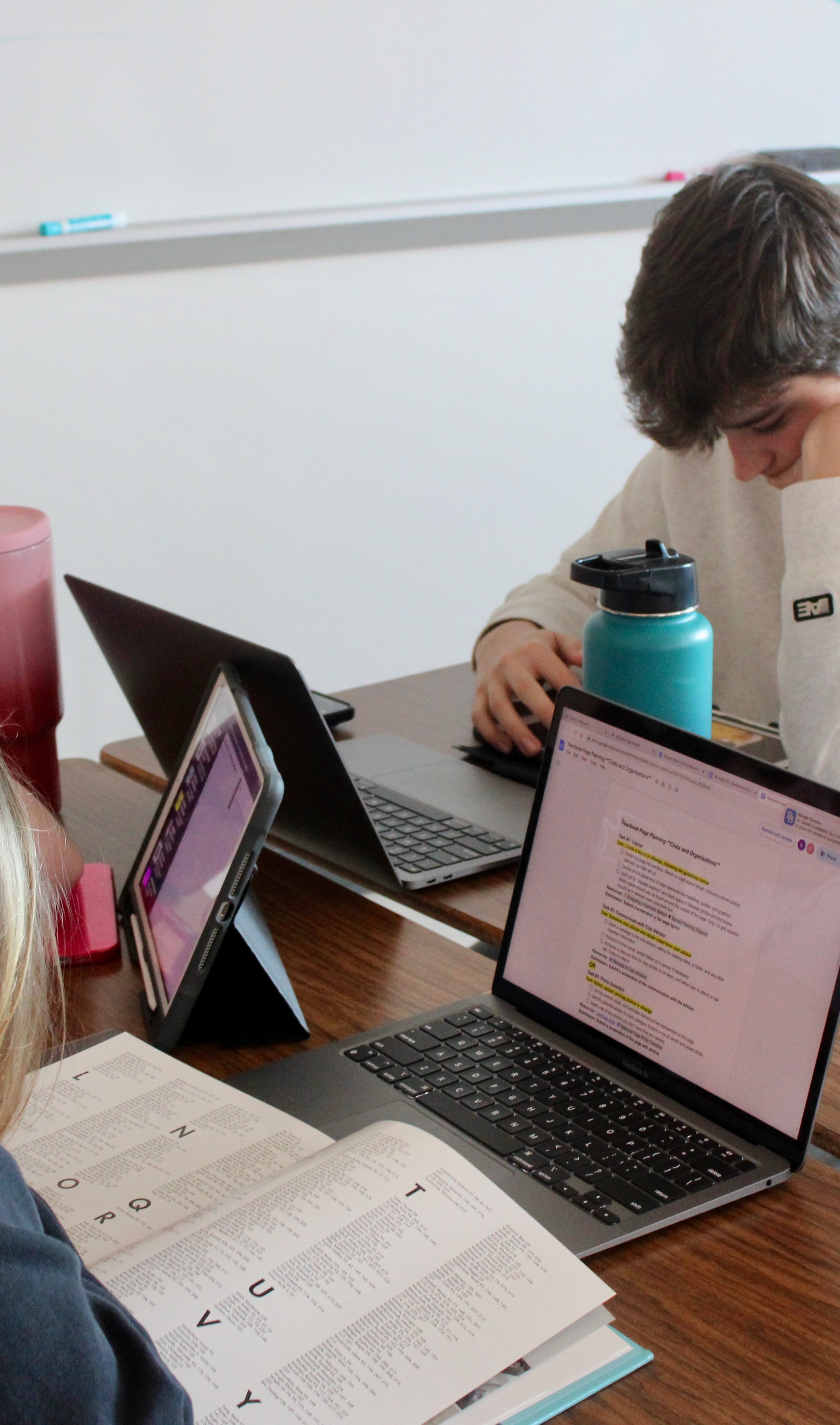 Students around a table working on laptops and tablets