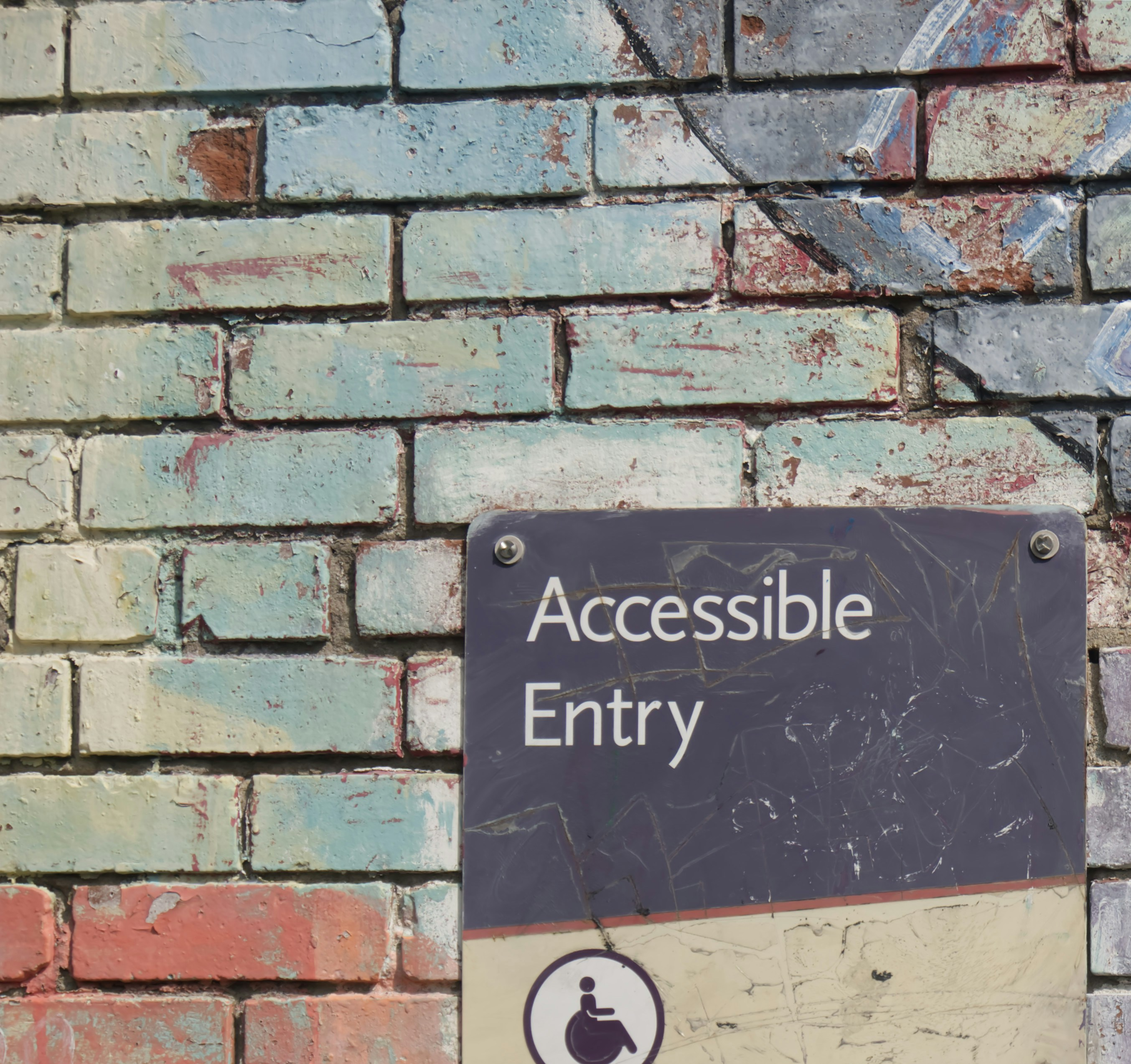 Multi-colored brick wall with a grey sign with white text "Accessible entrance"