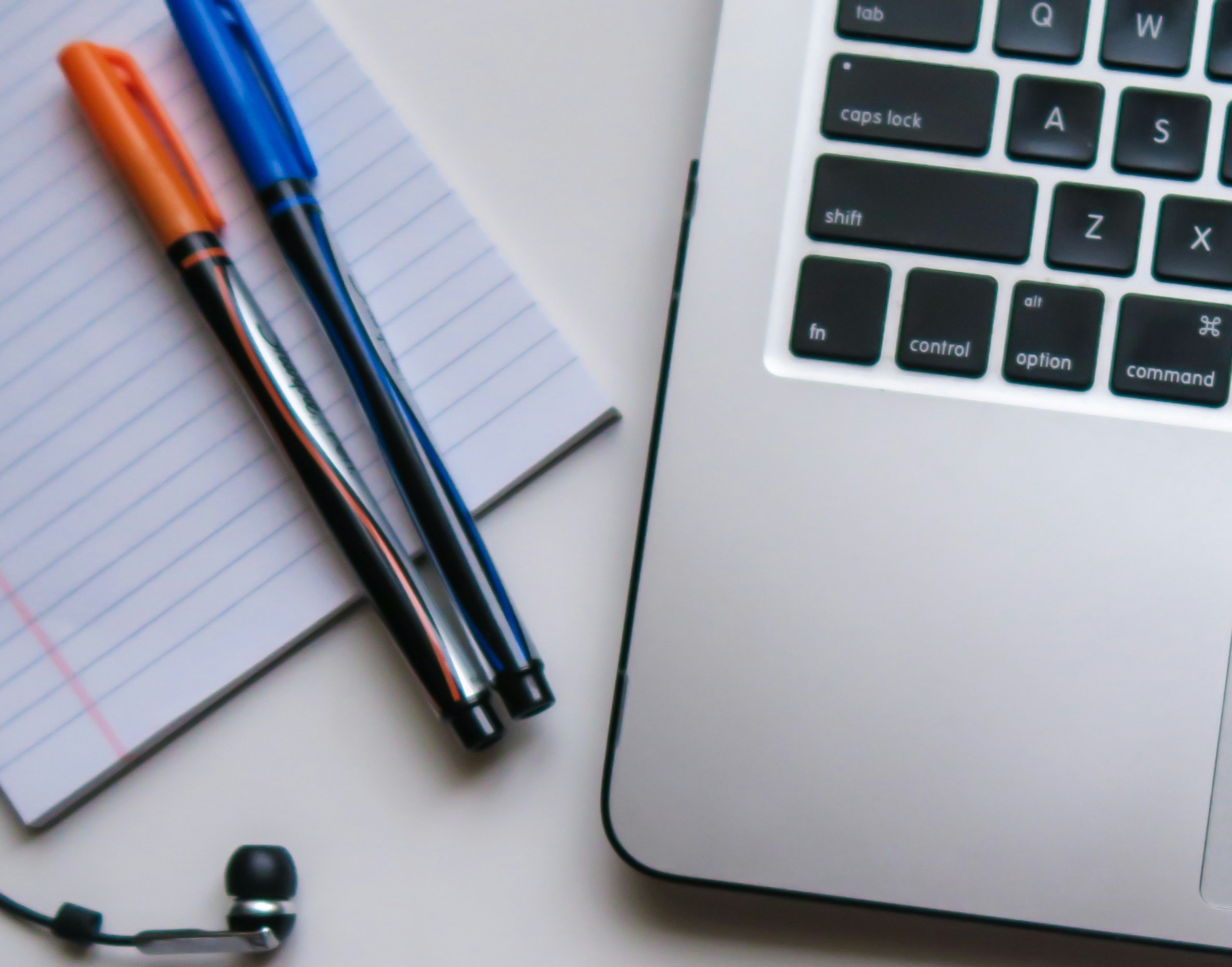 Open laptop, notebook, pens, and earbuds displayed on a table.