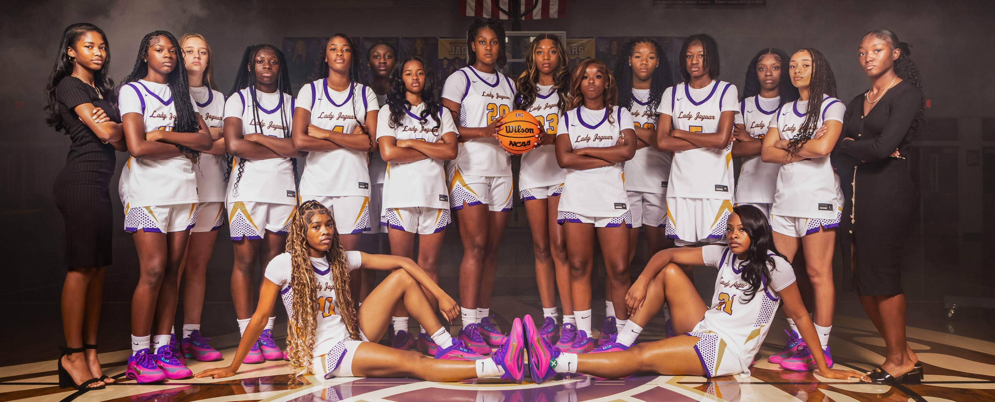 DCHS Lady Jags basketball team wearing black business semi-formal clothes, standing in a semicircle on the basketball court
