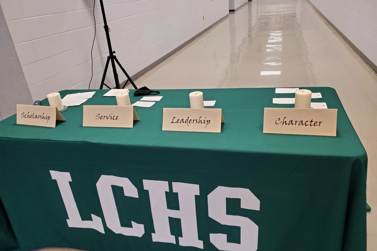 LCHS table with 4 candles on it with cards infront of each of them from left to right they say "Scholarship,Service,Leadership,Character