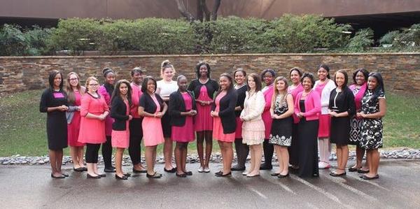 A group of young women stand together in black, pink and white outfits