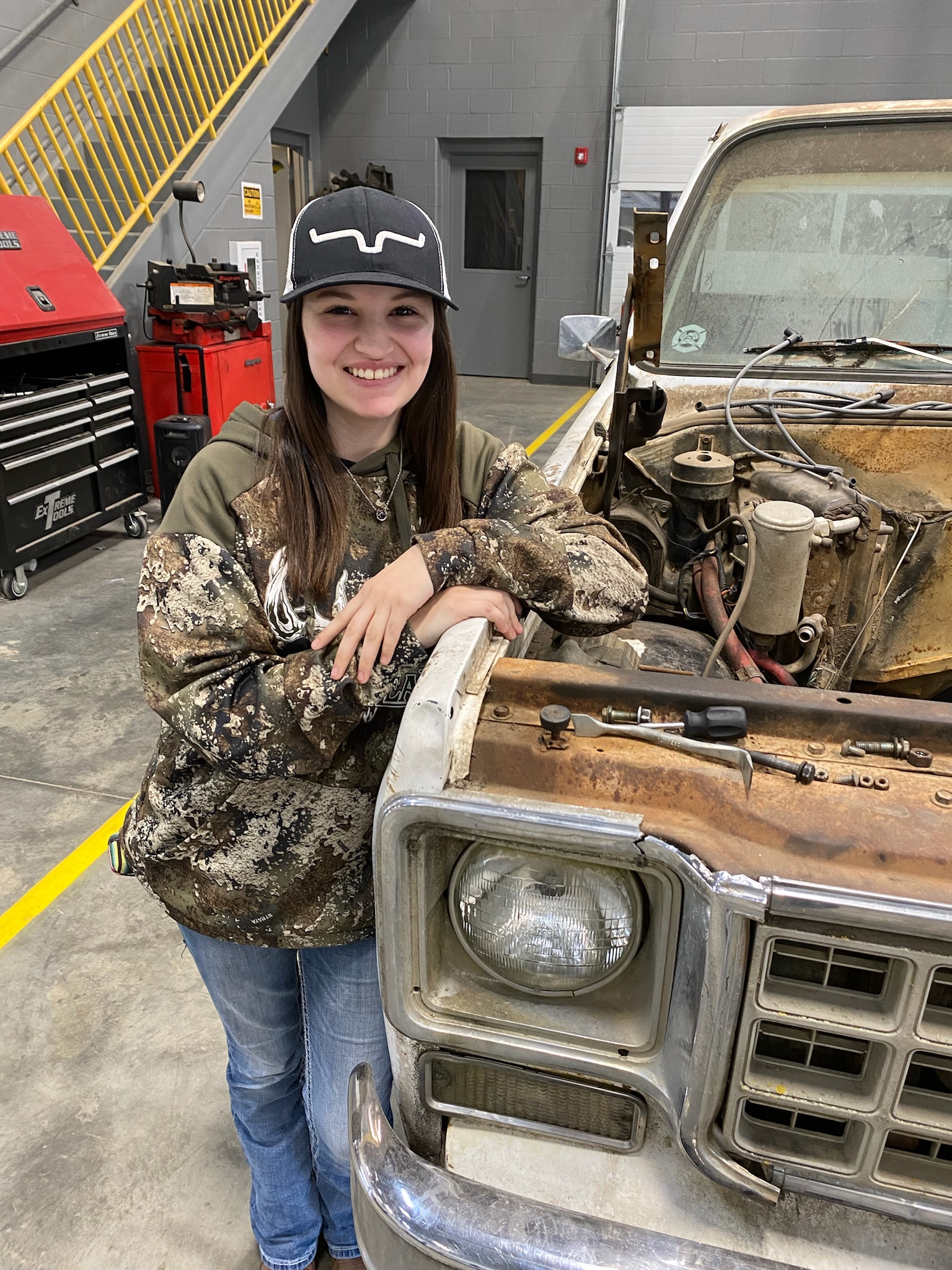 Student posing next to a truck with the hood off